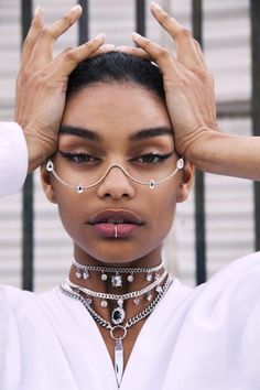 a woman is holding her hands up to her face and wearing a chain around her neck