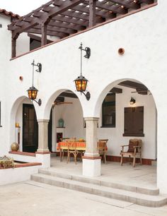 an outdoor dining area with chairs and tables in front of a white stucco building that has arched doorways