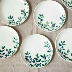 four white plates with green leaves and berries painted on the side, sitting on a table