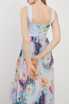 a woman in a floral print dress is holding her hand out to the side while looking down