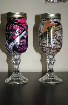 two glass vases sitting on top of a table next to each other, one painted pink and the other decorated with camo