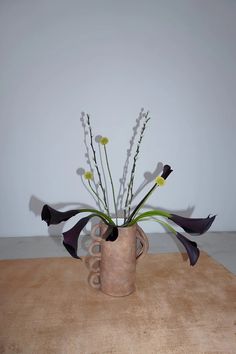 a vase filled with flowers sitting on top of a wooden table next to a wall