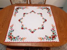 an embroidered tablecloth with flowers on it sits on a dining room table in front of two chairs