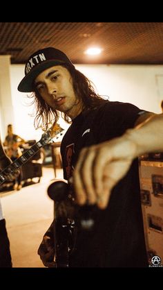 a man with long hair holding a guitar in his right hand and pointing at it