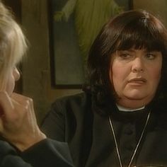 a woman sitting at a table talking to another woman with her hand on her head