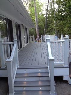 a white porch with steps leading up to the front door and back deck area that is surrounded by trees