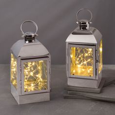 two gold lanterns with lights on them are sitting on a gray surface and one is lit up