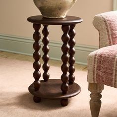 a vase sitting on top of a wooden stand next to a chair in a living room