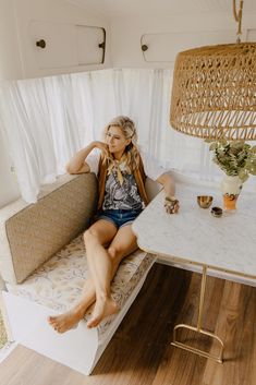 a woman sitting on top of a couch next to a white table and chair in a room