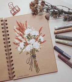 an open notebook with flowers on it next to crayon markers and pencils