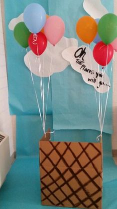 some balloons are floating in the air over a box on a blue tablecloth with a sign