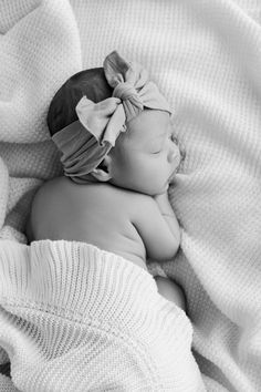 a black and white photo of a baby wrapped in a blanket with a bow on it's head