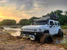 a white hummer truck is stuck in the mud with its lights on at sunset