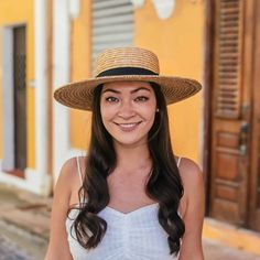 a woman wearing a straw hat standing in front of a yellow building