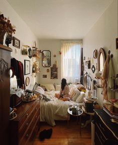 a woman sitting on a bed in a room with lots of clutter and decorations