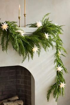 a fireplace decorated for christmas with greenery and white stars hanging from the mantel