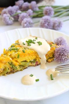 a white plate topped with an omelet covered in cheese and sauce next to purple flowers