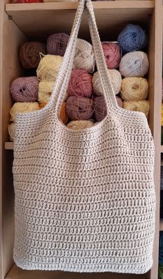 a white crocheted bag sitting on top of a wooden shelf filled with balls of yarn