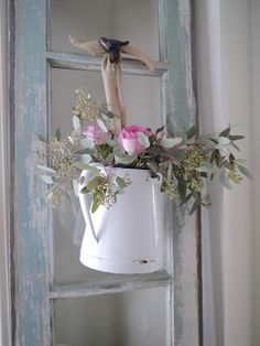 a white watering can filled with flowers on top of a window sill next to an old door