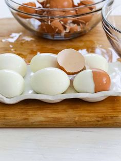 several eggs are in an egg shell on a cutting board next to a glass bowl