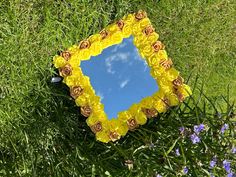 a yellow flowered mirror sitting in the grass with blue sky and clouds behind it