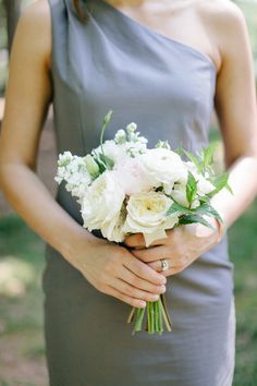 a woman in a gray dress holding a white bouquet and wearing a ring on her finger