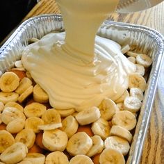 a pan filled with bananas and cream being drizzled on top of it