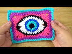 someone is holding up a crocheted square with an evil eye on the center