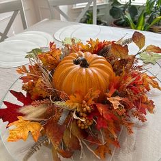 a glass bowl filled with lots of leaves and a pumpkin on top of a table