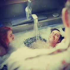 two people in a bathtub with water running from the faucet