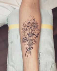 a woman's arm with flowers on it and a bow around the wrist tattoo