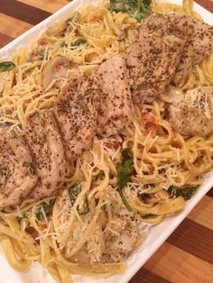 a white plate topped with pasta and meat covered in sauces on top of a wooden table