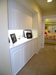 an empty room with white cabinets and pictures on the wall, along with a bed in the background