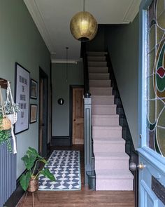 a hallway with stairs and tiled flooring next to a potted plant on the ground