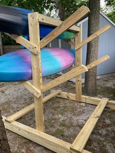 a blue and pink surfboard sitting on top of a wooden stand next to a tree