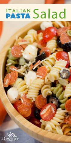 a pasta salad with tomatoes, olives and mushrooms in a wooden bowl on top of a table