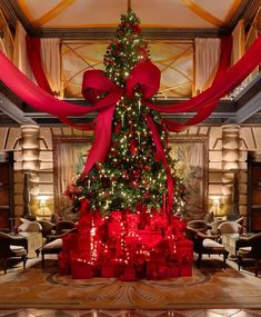 a large christmas tree with red bows and presents under it in a room filled with chairs