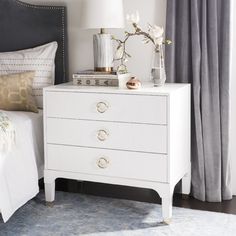 a white dresser with two drawers and a lamp next to it on top of a bed