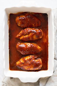 three pieces of meat in a white casserole dish with sauce on the side