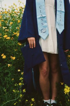 a woman wearing a blue graduation robe standing in flowers