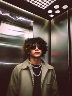 a man with curly hair and sunglasses standing in front of a metal elevator stall door