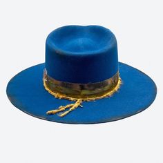 Soak up the beautiful deep blues and dream of the Mediterranean in the Aegean Fedora Hat. A medium distressed teal blue felt with hand dyed silk trimmings dressed with golden details and designs. Designed to be worn Summer to Winter. All hats are created, shaped and detailed by Valeria Andino in her Studio. Medium distressed felt Quartz crystal points Silk thread with 18k gold square wire ring 24k gold plated crimp beads 18k pinky gold filled bar chain Smoke topaz Swarovski chatons 18k gold over Ceremonial Blue Adjustable Hat, Adjustable Blue Ceremonial Hats, Vintage Blue Adjustable Hat Bands, Blue Felt Hat With Short Brim For Rodeo, Blue Wide Brim Hat For Festival, Fitted Blue Western Fedora, Luxury Blue Short Brim Hat, Elegant Blue Felt Hat With Flat Brim, Blue Western Felt Hat With Short Brim