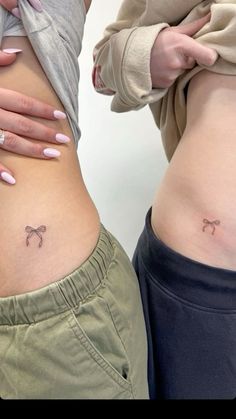 two women with tattoos on their stomachs and one has a small bow at the bottom