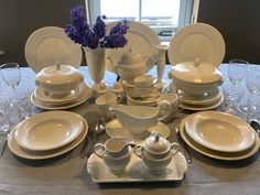 the table is set with dishes, cups and saucers in white on gray linens