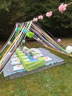 a picnic table with balloons and streamers on the grass in front of some trees