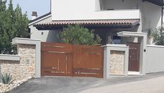 a white house with brown wooden doors and stone fenced in area next to it