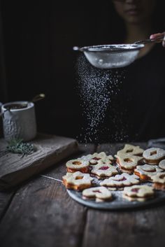 a person sprinkling sugar on pastries on top of a wooden table next to a bowl