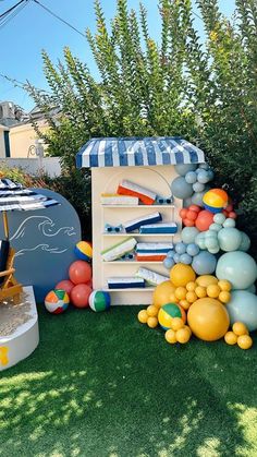 an assortment of balloons and toys on the grass in front of a building with a blue striped awning