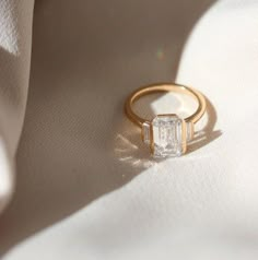 a diamond ring sitting on top of a white sheet with sunlight coming through it's shadow