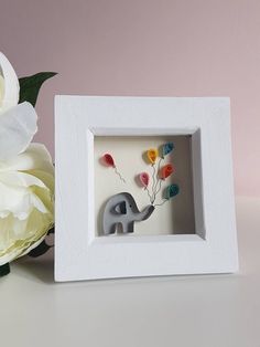 an elephant with balloons in its trunk is sitting next to a white flower and vase